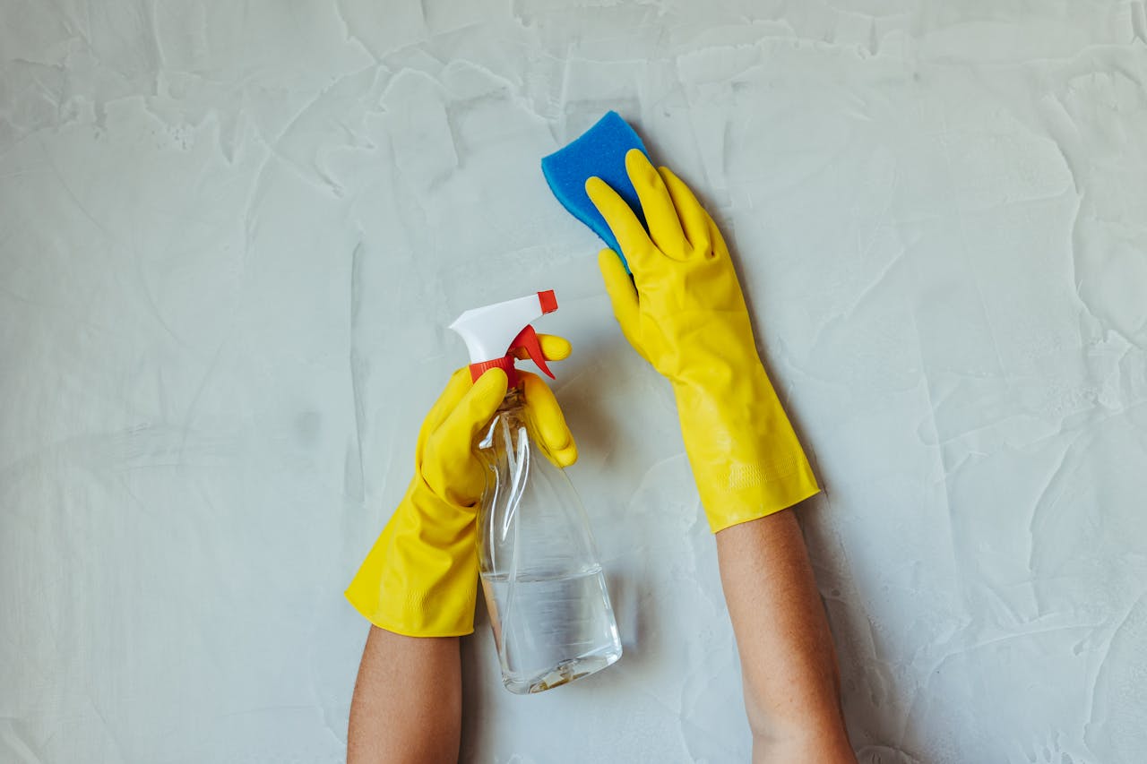 why-choose-us Close-up of hands in yellow gloves cleaning a wall with a spray bottle and sponge.